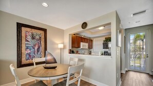 A dining area with a round table and chairs, a kitchen with cabinets and appliances, and a door leading outside. - Mangrove View 2BR - Pool Hot Tub Gym Access (Ruskin)
