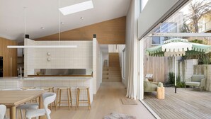 A modern kitchen with a wooden ceiling, a dining area with a wooden table and white chairs, and a patio with outdoor furniture and a green umbrella. - Bridgewater House Gas Heated Pool (Melbourne)