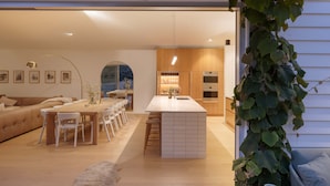 A modern kitchen with wooden cabinets, a central island, and a dining area with a sofa and chairs. - Bridgewater House Gas Heated Pool (Melbourne)