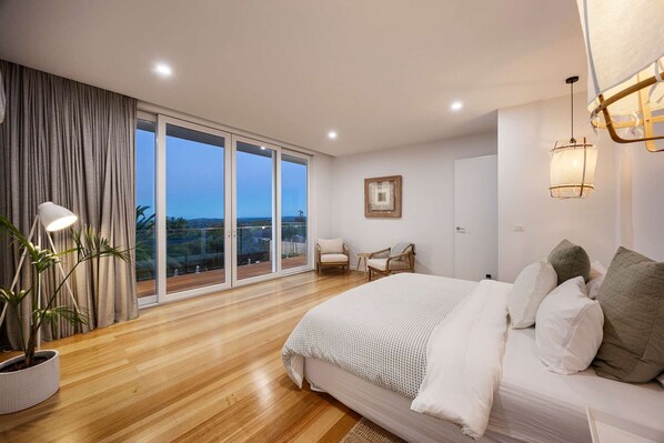 A bedroom with a large bed, a potted plant, a chair, and a view through a sliding door. - Airosa Blanca Pool Spa Sea Views (Melbourne)