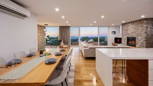 Ein modernes Wohnzimmer mit Kamin aus Stein, einem Essbereich mit Holztisch und -stühlen sowie einem großen Fenster mit schöner Aussicht.
