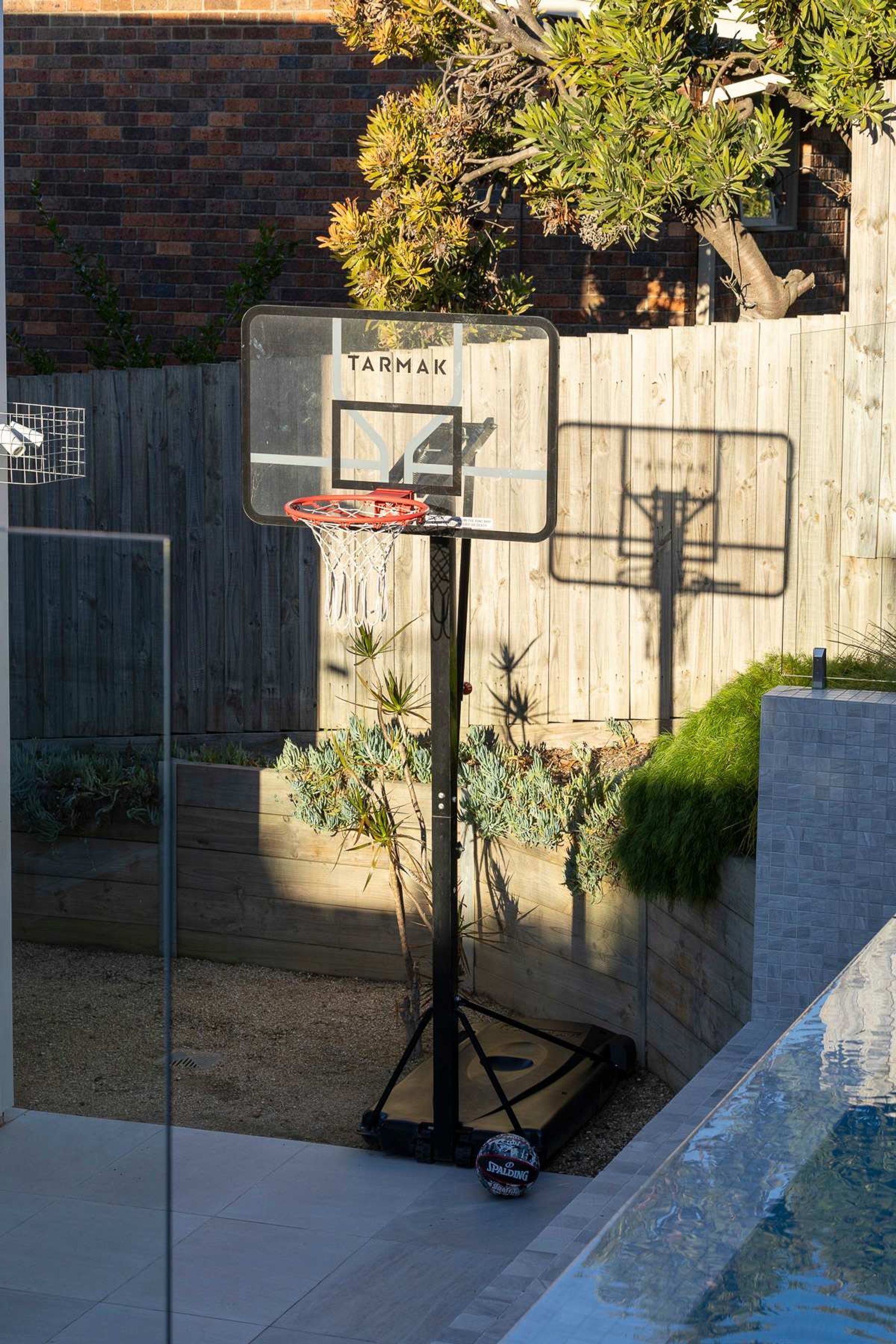 A basketball hoop with a sign, a wooden fence, and a small pool in a backyard.