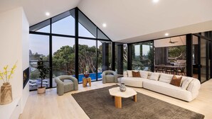 Een moderne woonkamer met een groot raam, een bank, fauteuils, een salontafel en een open haard.