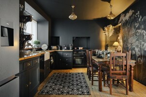 A modern kitchen with dark cabinetry, a wooden dining table, and a chandelier.
