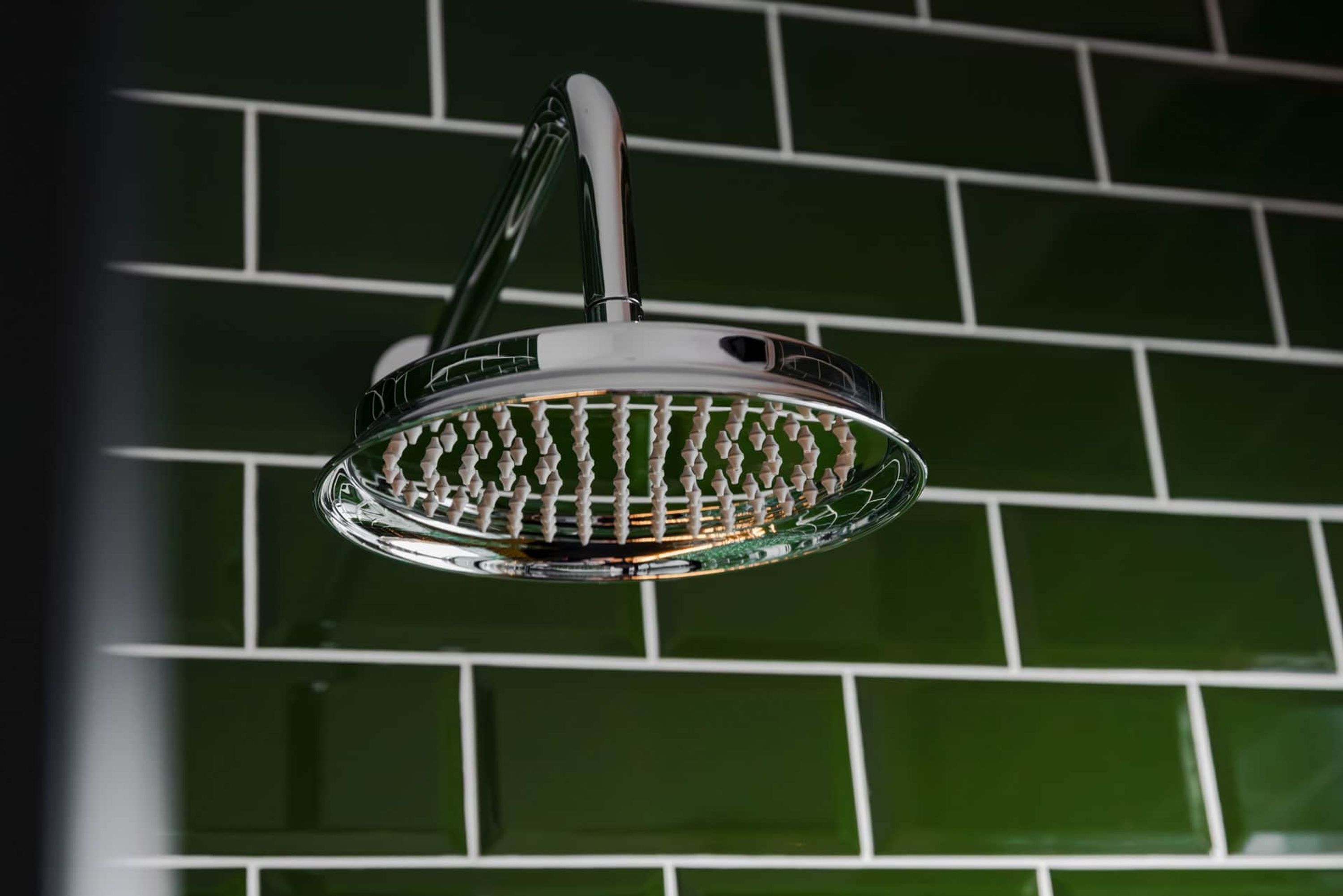 A showerhead with a chrome finish and a white handle, mounted on a green tiled wall.