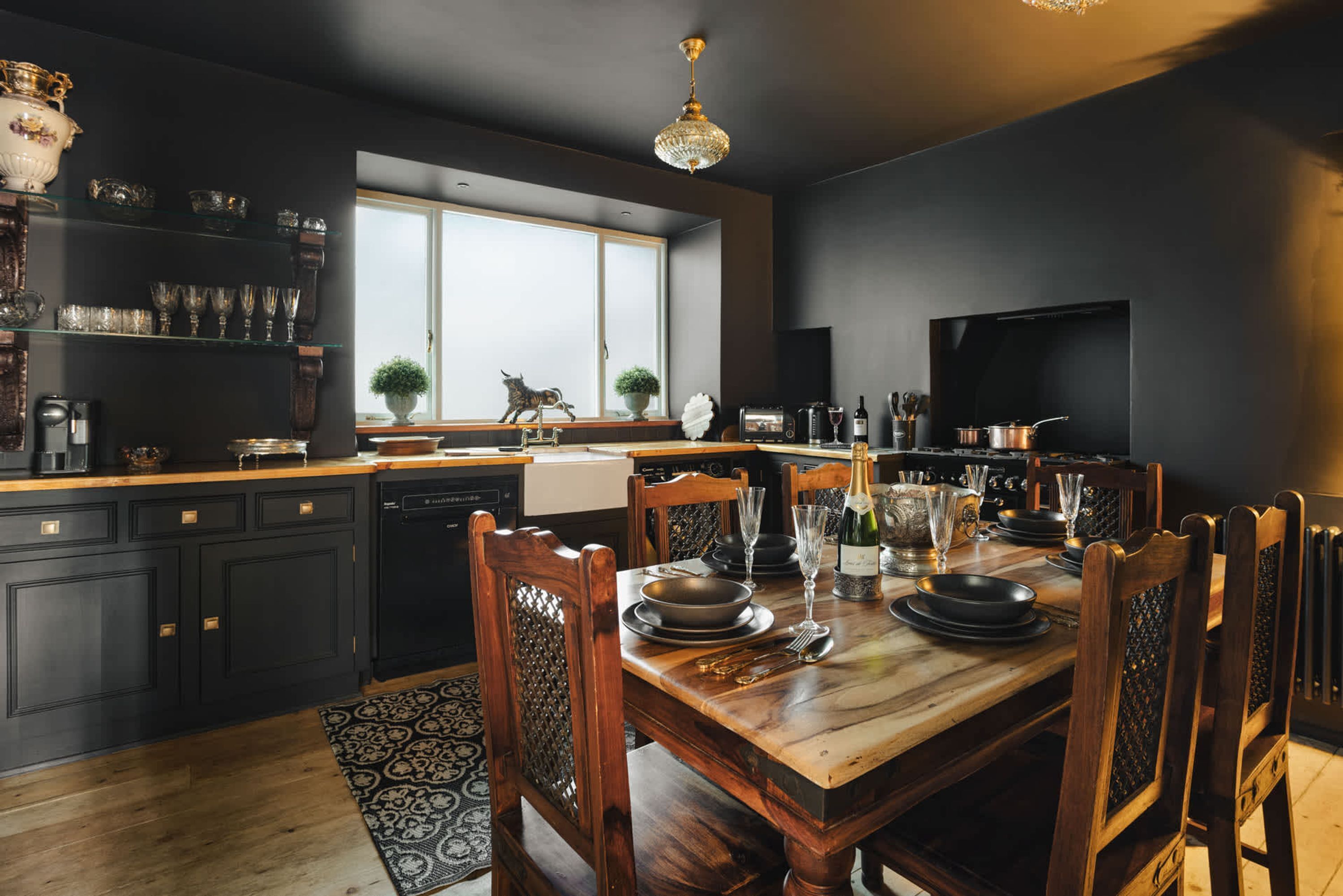 A modern kitchen with dark cabinetry, a wooden dining table, and a large window.