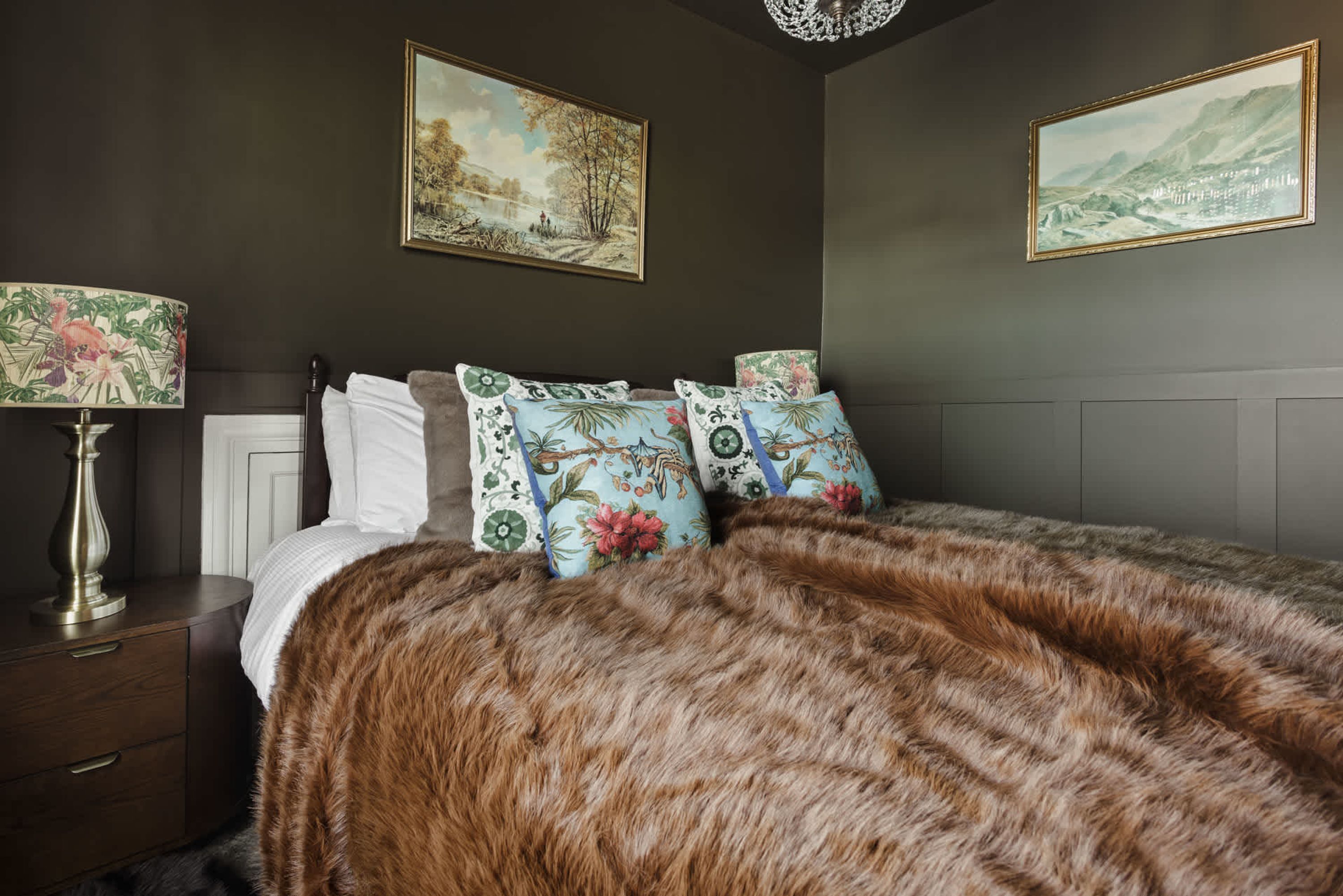 A bedroom with a bed, nightstands, a lamp, and two paintings on the wall.