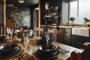 A dining area with a wooden table set for a meal, a staircase, and a kitchen area with shelves.