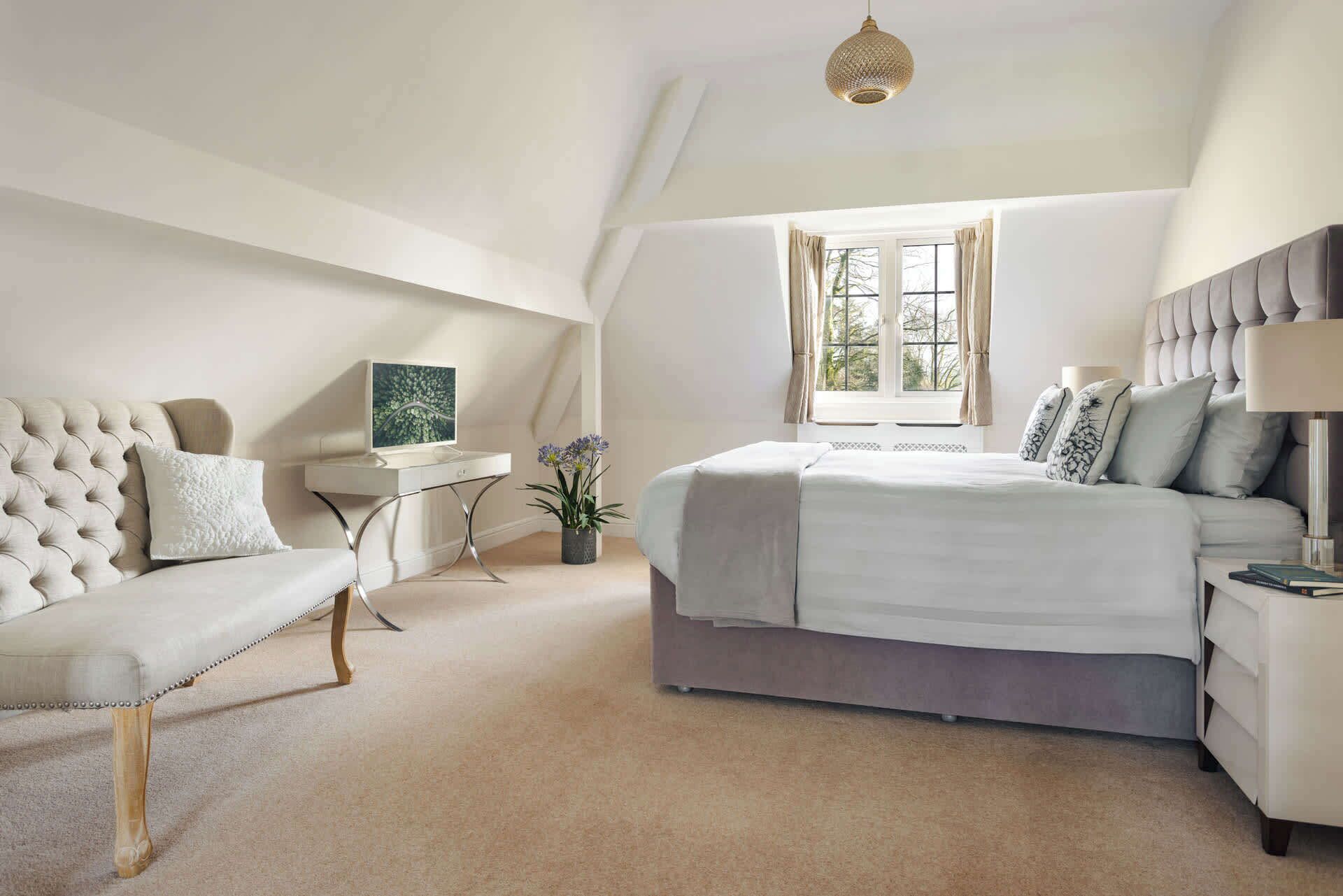 A bedroom with a bed, a bedside table, a chair, a window, and a hanging light fixture.