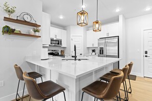 A modern kitchen with a large island, bar stools, pendant lights, and built-in appliances. - Keystone Condo With Pool (Keystone)