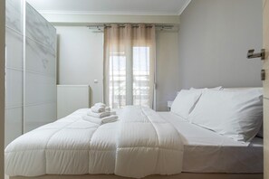 A bedroom with a bed, a radiator, and a window with curtains. - Faliro Escape - Spacious Stay in Thessaloniki (Thessaloniki)