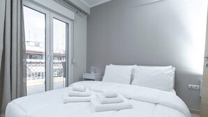 A hotel room with a bed, a nightstand, and a view through a sliding door. - Faliro Escape - Spacious Stay in Thessaloniki (Thessaloniki)