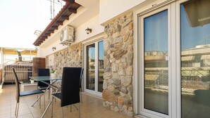 A patio with a table and chairs, stone walls, and large sliding glass doors. - Faliro Escape - Spacious Stay in Thessaloniki (Thessaloniki)
