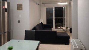 A modern kitchen with a refrigerator, a dining table with a glass top, and a black sofa. - Faliro Escape - Spacious Stay in Thessaloniki (Thessaloniki)