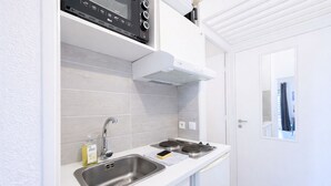 A compact kitchenette with a stainless steel sink, a stove, and a microwave above the counter. - T2 balcony with barbecue, Tennis MC (Beausoleil)