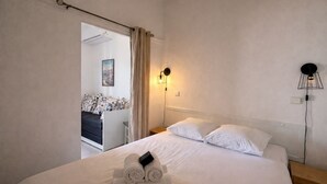 A hotel room with a bed, a nightstand, a wall-mounted lamp, and a door leading to another room. - T2 balcony with barbecue, Tennis MC (Beausoleil)