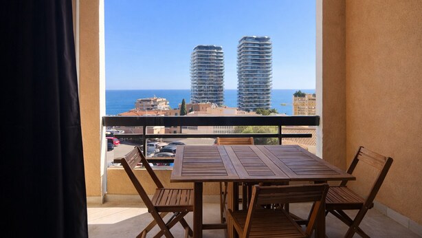 A balcony with a table and chairs, overlooking a cityscape with tall buildings and a clear sky. - T2 balcony with barbecue, Tennis MC (Beausoleil)