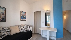 A modern living room with a black sofa, patterned cushions, a white table, and a framed cityscape poster. - T2 balcony with barbecue, Tennis MC (Beausoleil)