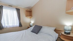 Un letto rifatto con cura, lenzuola a righe, una lampada da comodino e una finestra con tende.
