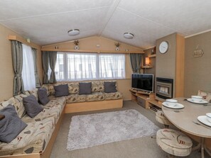 A cozy RV interior with a sofa, TV, fireplace, dining table, and curtains. - Ger Y Mor (New Quay)