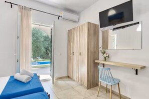 Ein Hotelzimmer mit Bett, Sessel, Fernseher, Kleiderschrank und Blick auf einen Pool.