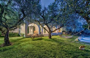 Ein gepflegter Garten mit Terrasse, Schwimmbad und einem Haus mit Arkaden.