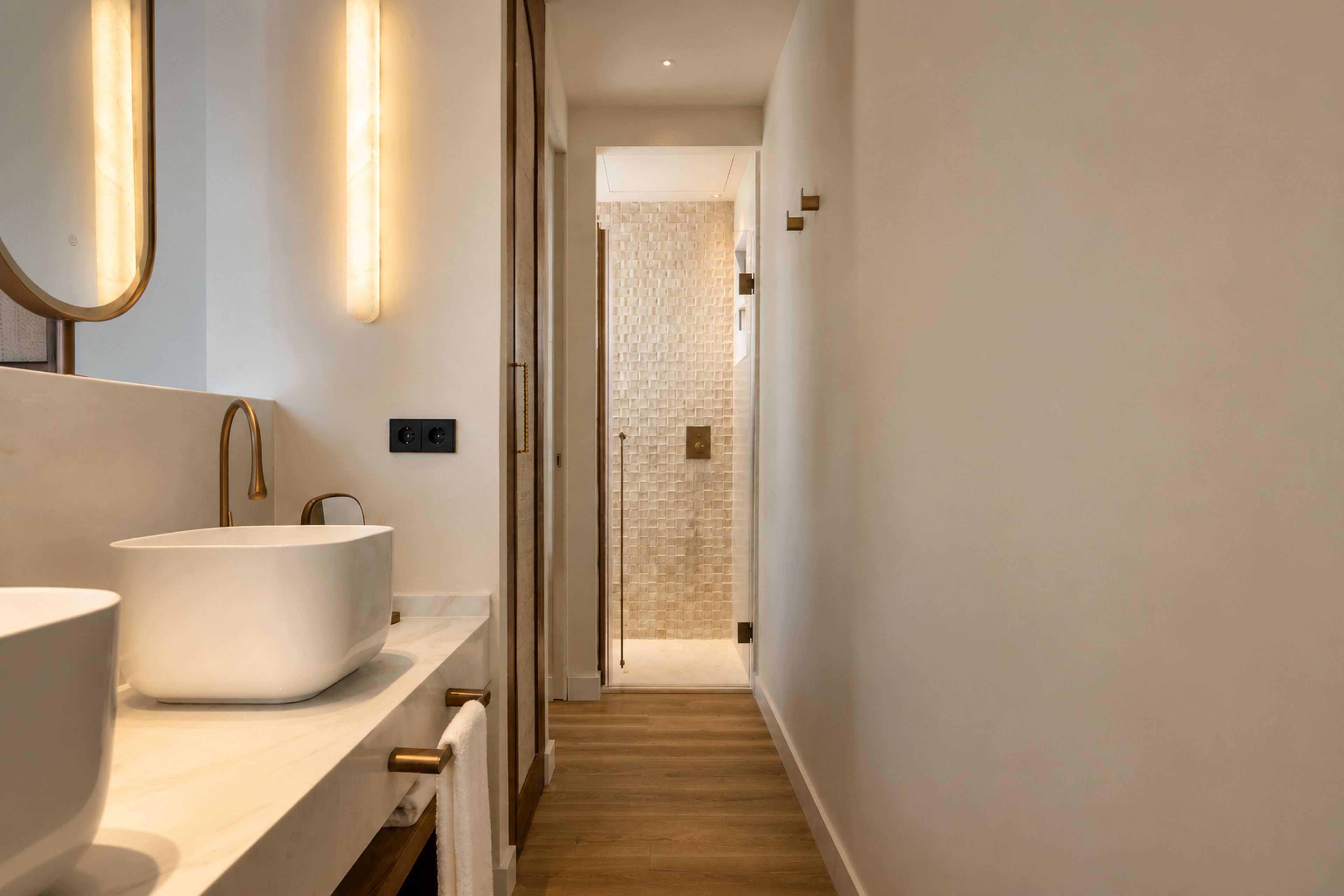 Un bagno moderno con un ampio lavandino bianco, uno specchio con cornice dorata e un pavimento in legno.