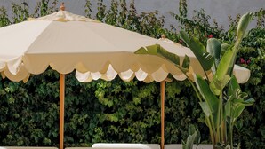 A poolside area with a white sofa, a table, a potted plant, and a large umbrella. - CASA METT Sitges - Adults Only (Sitges)