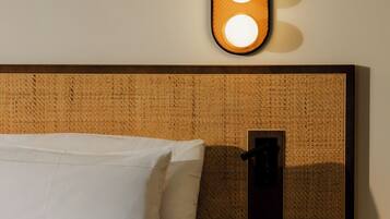 A neatly made bed with white linens, a bedside table with a water bottle and glasses, and a wall-mounted light fixture with two illuminated bulbs.