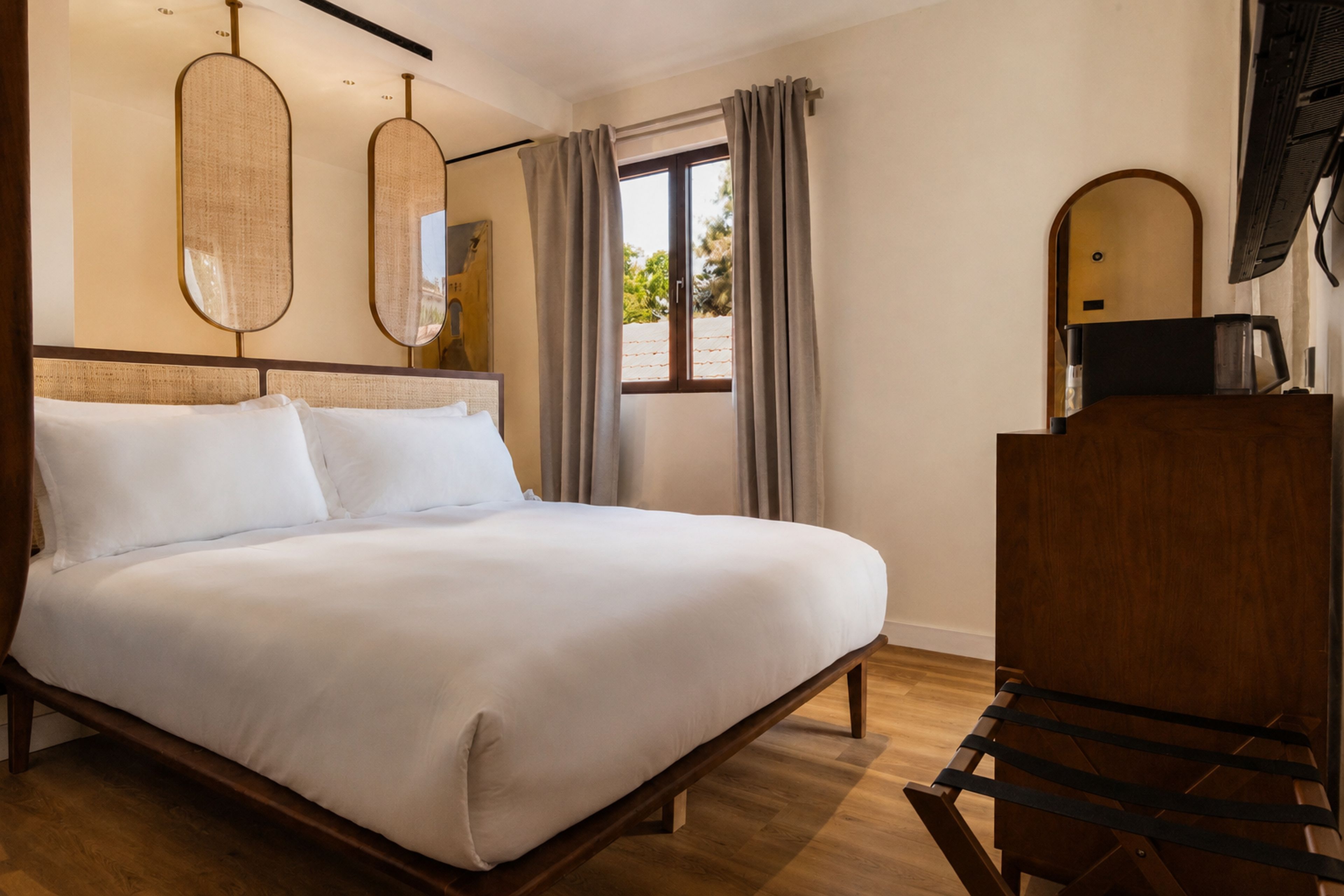 A hotel room with a large bed, wooden headboard, a desk with a chair, and a window with curtains.
