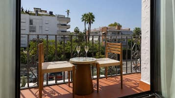 Uma varanda com duas cadeiras e uma mesa, com vista para um horizonte urbano com edifícios e palmeiras.