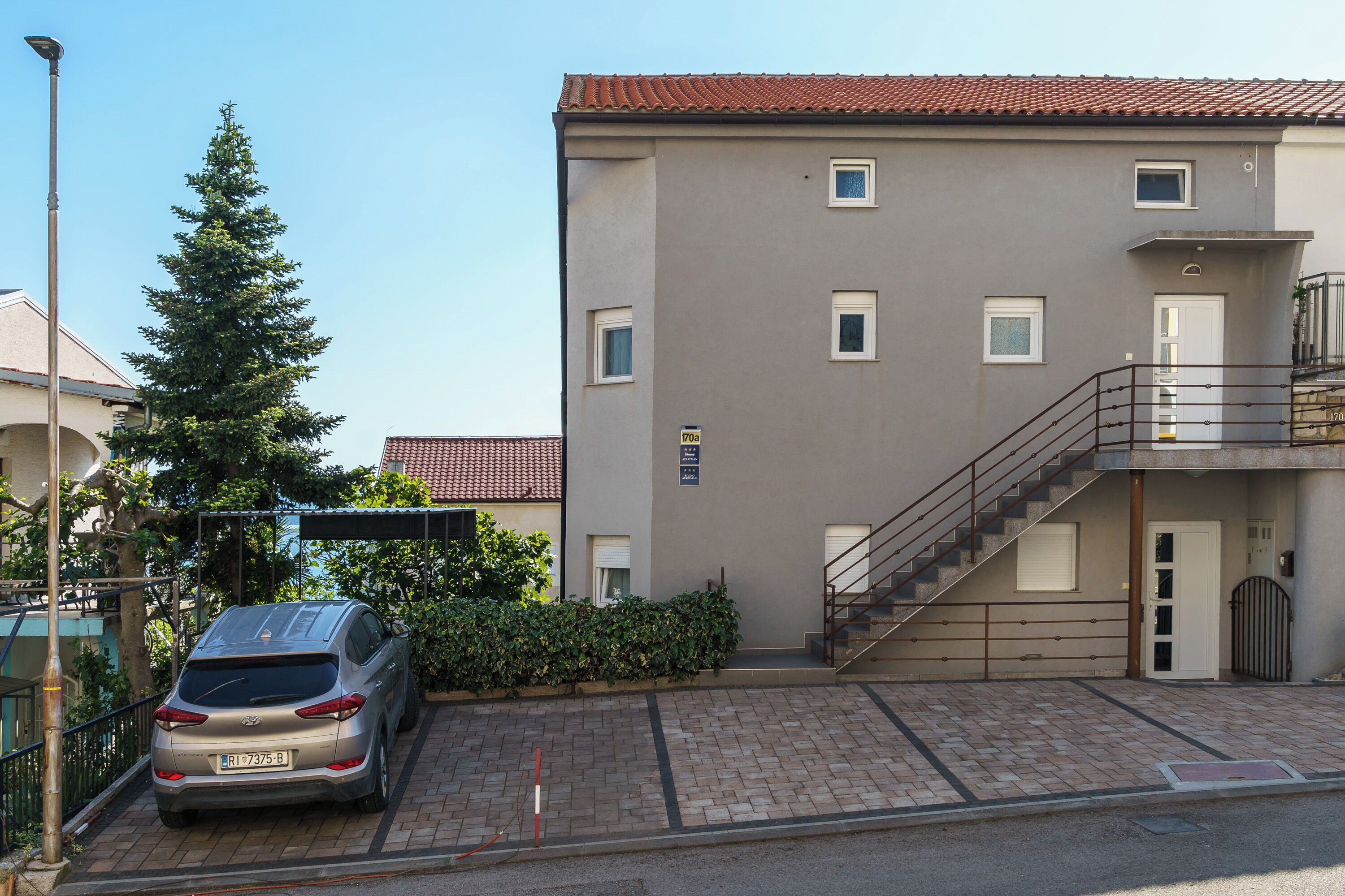 A building with a car parked in front, a staircase, and a clear sky.