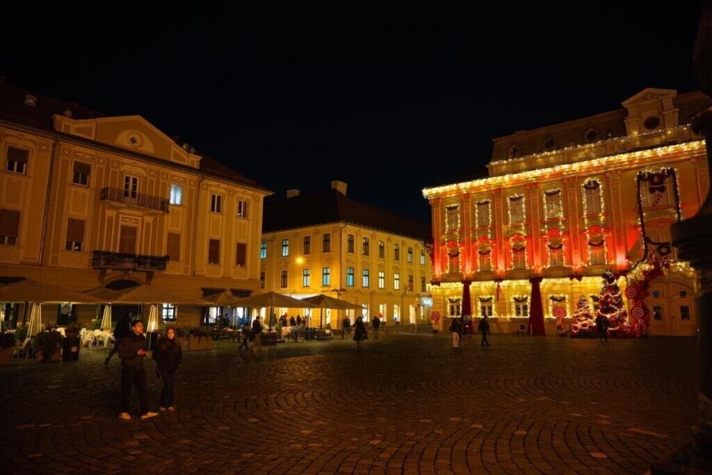 A historic building with ornate architecture, a cobblestone plaza, and festive lights.