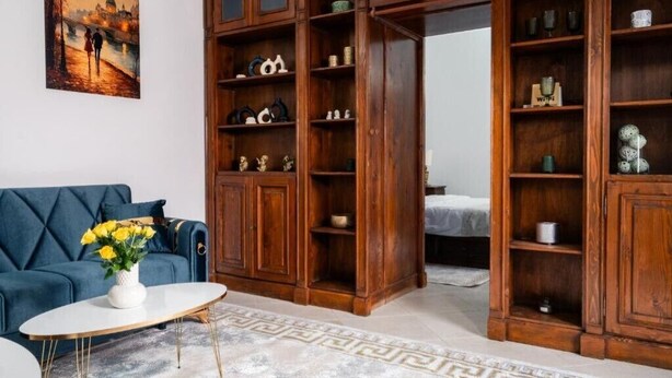 Une pièce avec un canapé bleu, une table basse blanche, un tapis à motifs et des étagères en bois sur lesquelles sont disposés divers objets.