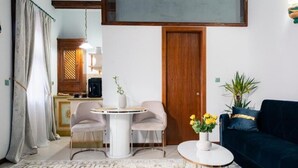 Un salon comprenant une table ronde, deux chaises, un canapé, une table basse, un meuble et une porte.
