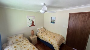 Quarto com duas camas, um ventilador de teto e uma porta de madeira.