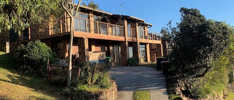 A two-story building with a balcony, a stone retaining wall, and a pathway leading to the entrance.