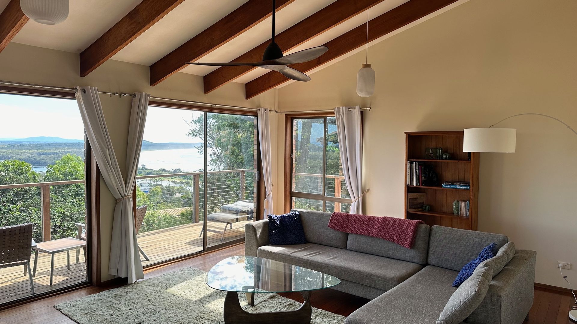 A spacious living room with a large glass door leading to a balcony, a sofa, a coffee table, and a bookshelf.
