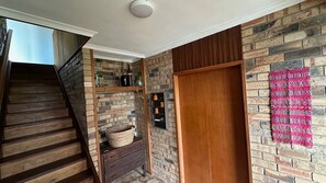 Escadaria que dá acesso a um quarto com parede de tijolos, porta de madeira e prateleiras com diversos objetos.