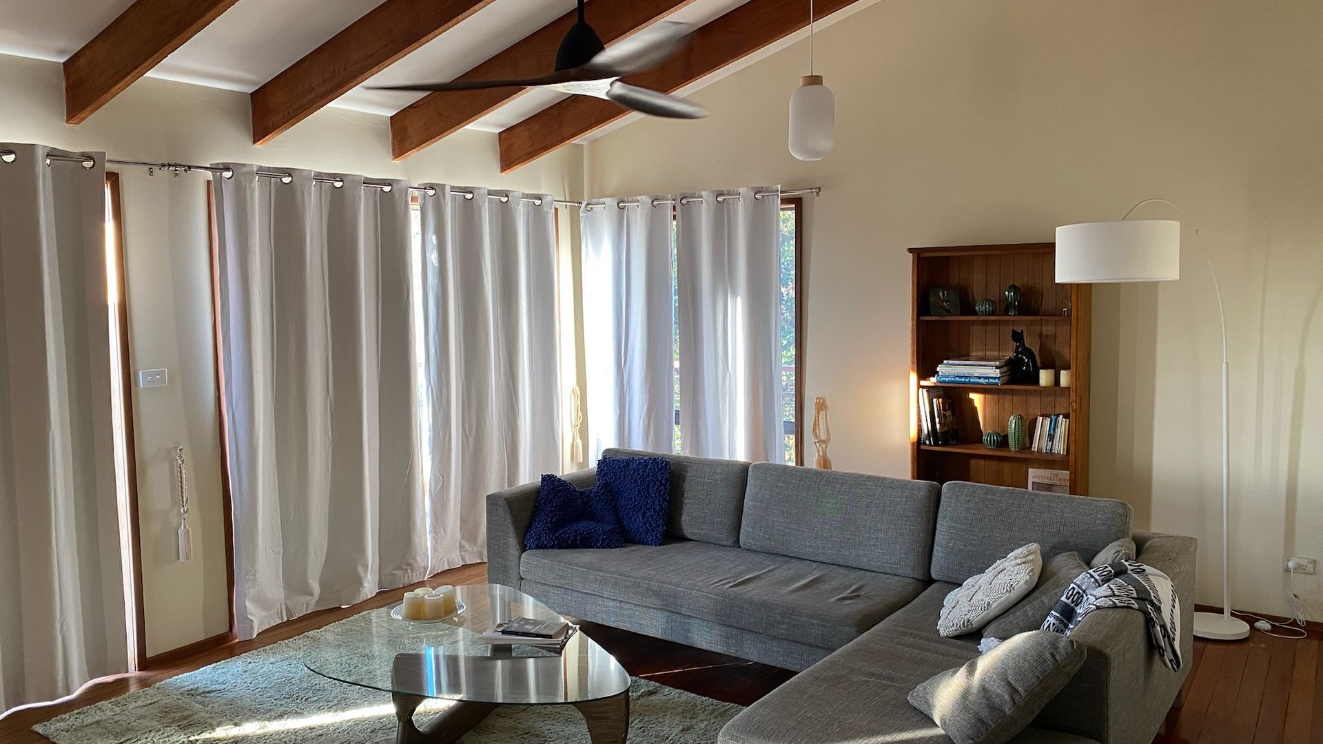 A living room with a grey sofa, a glass coffee table, and a bookshelf.