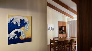 A dining area with a wooden table and chairs, a wall-mounted sign reading 'FULL', and a large artwork depicting a wave.