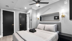 Ein modernes Schlafzimmer mit Bett, Deckenventilator, Nachttisch, Wand-Fernseher und einer Tür.