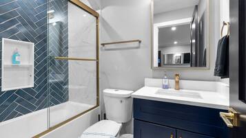 A modern bathroom with a glass-enclosed shower, a white toilet, a vanity with a sink, and a mirror.