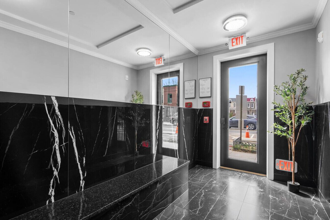 A modern lobby with marble flooring, a reception desk, and two exit signs.
