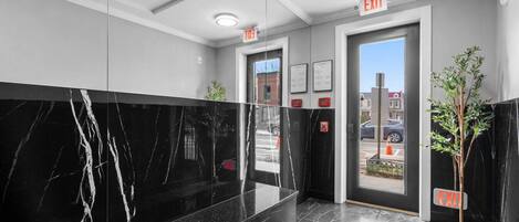 A modern lobby with marble flooring, a reception desk, and two exit signs.