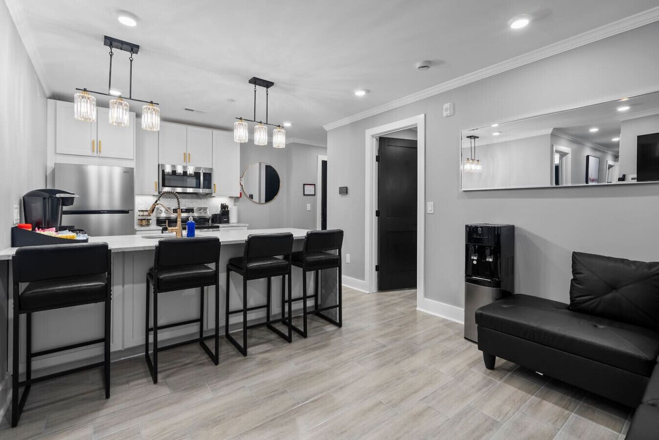 Une cuisine moderne avec un îlot central, des tabourets de bar, un canapé noir et un grand miroir.