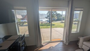 Quarto com mesa de jantar, cadeiras, sofá e porta de vidro deslizante que dá para um pátio com vista para a rua e vegetação.