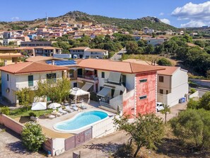 A residential building with a swimming pool, multiple balconies, and a view of a hillside town. - Residence Il Ciliegio with swimming pool - Apartment 6 (Trinity of Agultu)