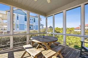 A covered outdoor area with a wooden table and benches, large windows offering views of neighboring houses and greenery. - Welcome to The Ruby Pearl! (St. George Island)