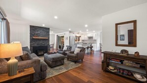 A spacious living room with a fireplace, a dining area, and a kitchen in the background. - Hayden Lake Home w/ Studio Suite & 2 Living Areas (Hayden Lake)